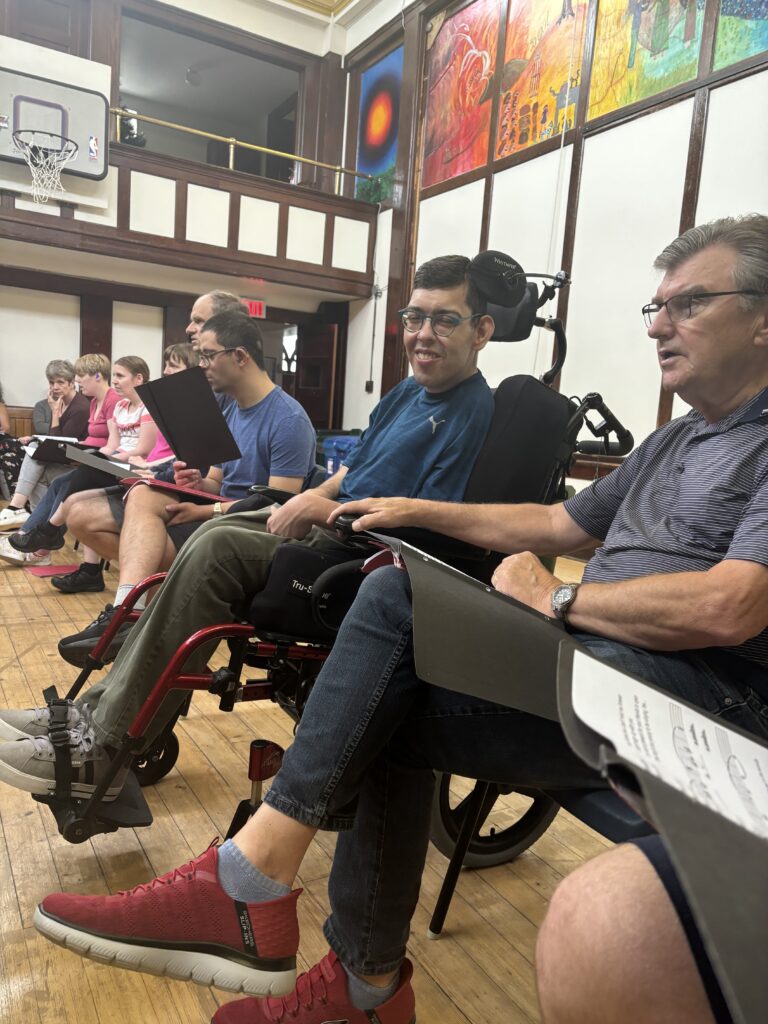 group of people sitting together, reading music and singing at a choir event.