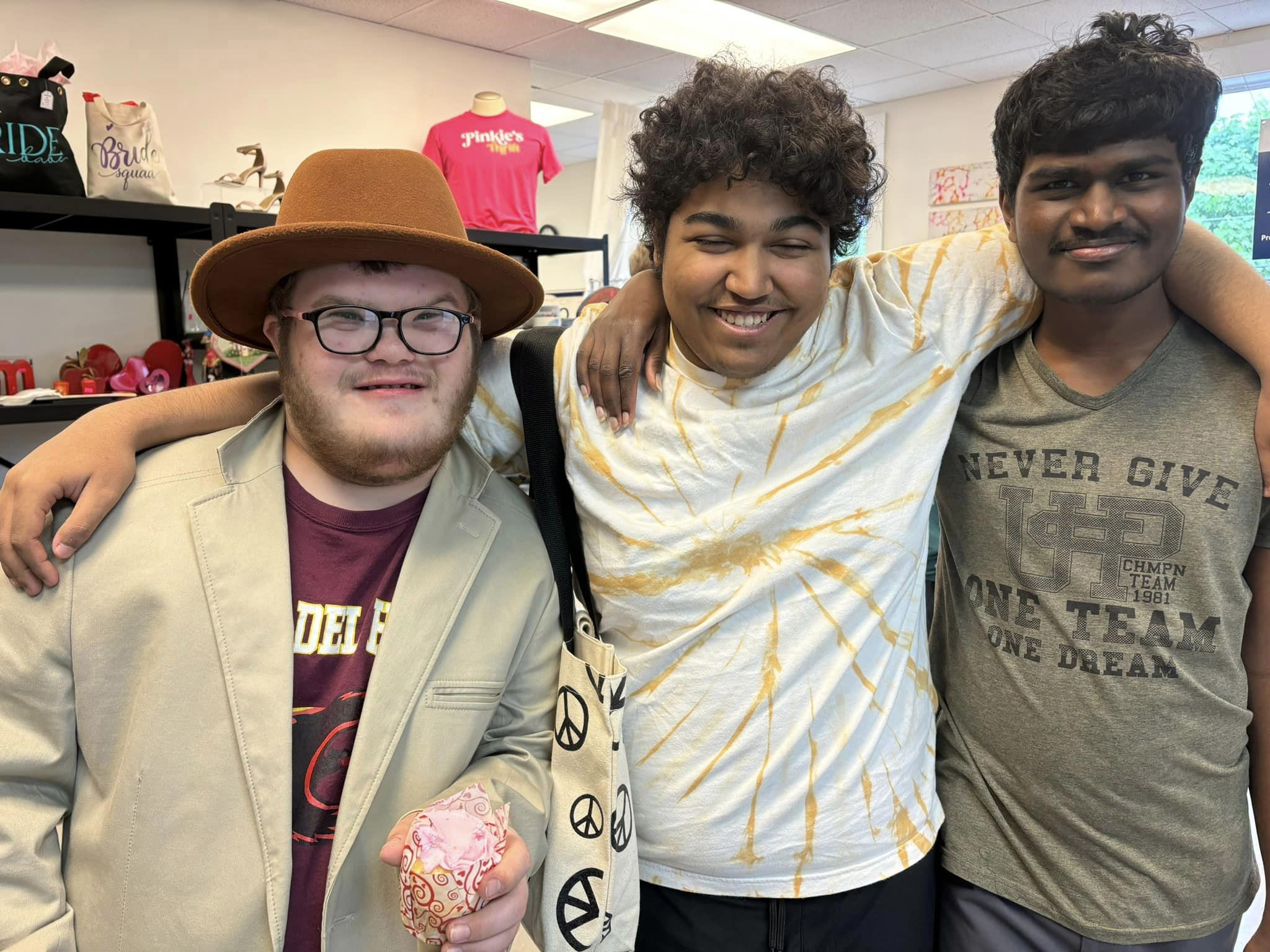 Group of 3 members smiling together inside Pinkie's Thrift shop