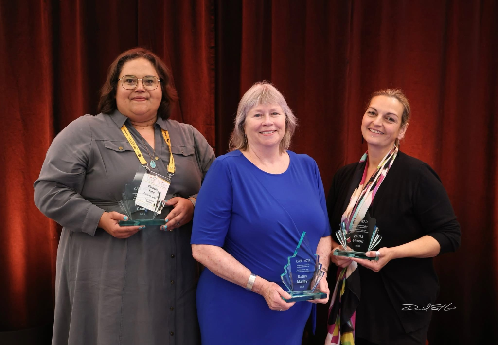 three people stand together on stage after accepting their awards