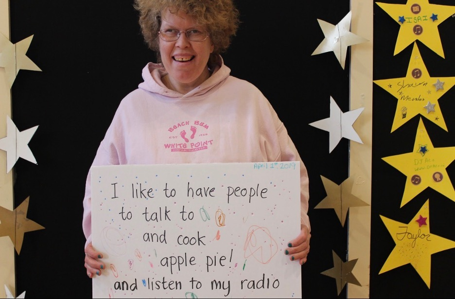 Beth MacLean advocates for the rights of people with disabilities, holding a sign that reads "I like to have people to talk to and cook apple pie! and listen to my radio".
