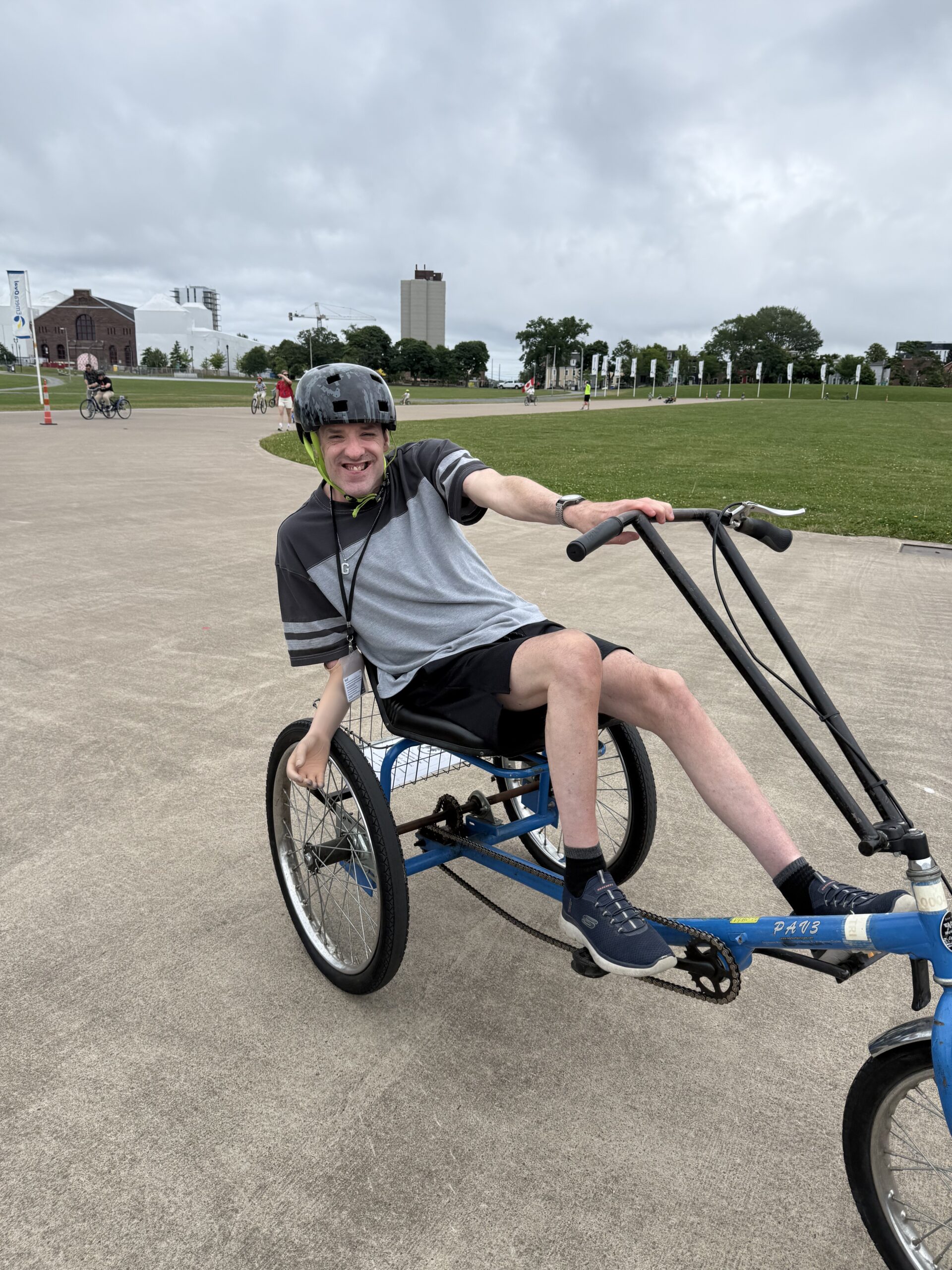 person happily rides a full-seat accessible bike while wearing a helmet around an outdoor path